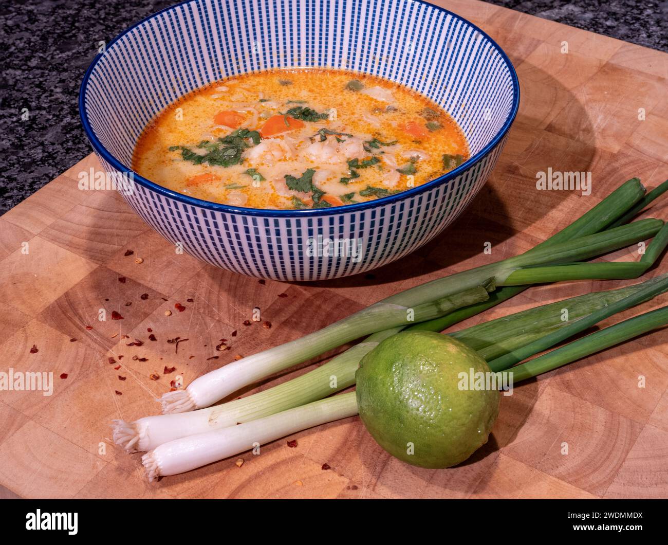 Savor the rich flavors of a zesty Asian coconut soup infused with red curry paste, elegantly presented in a blue bowl atop a wooden block. Accompanied Stock Photo