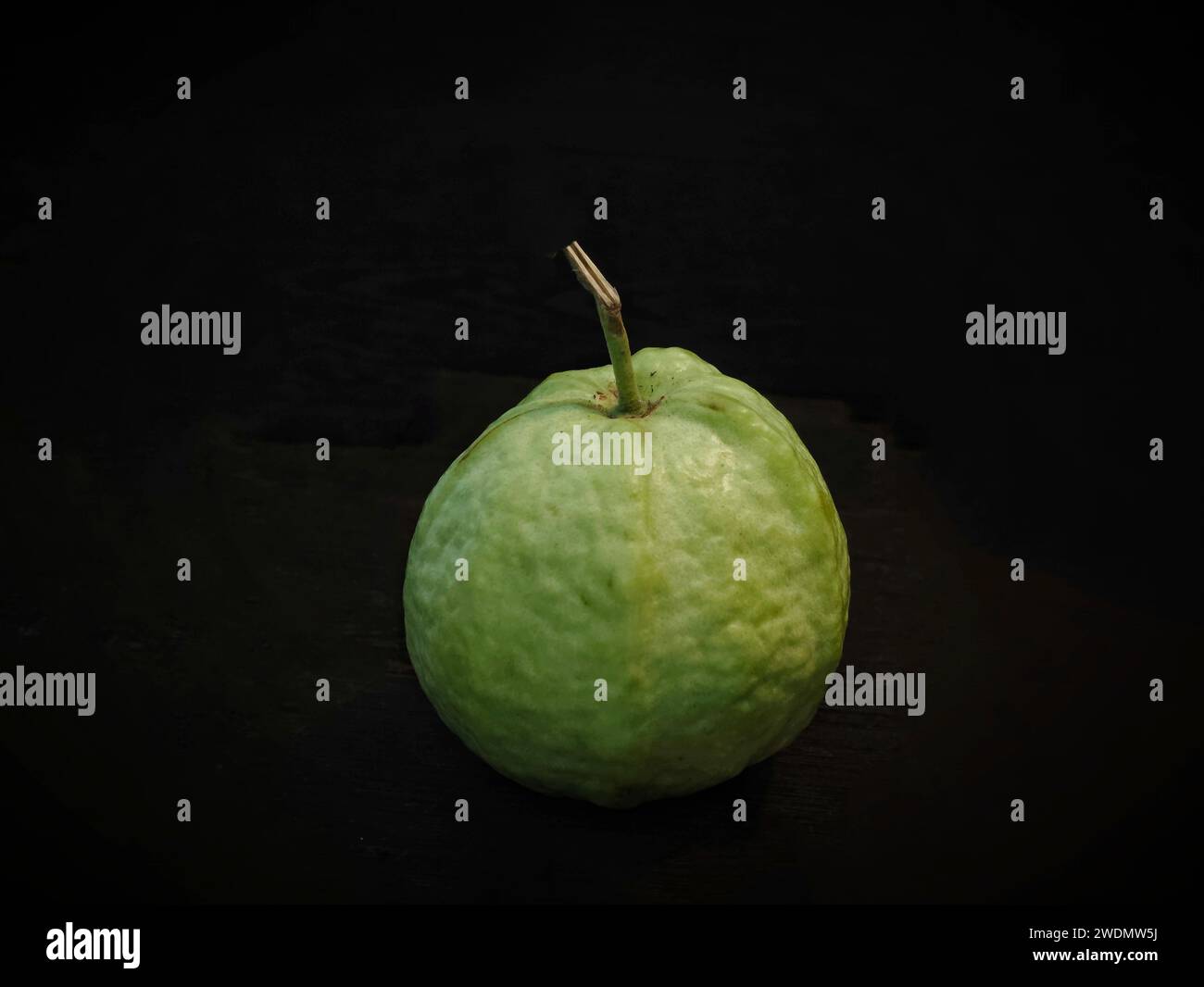 A single guava fruit showcased against a sleek black backdrop, casting ...