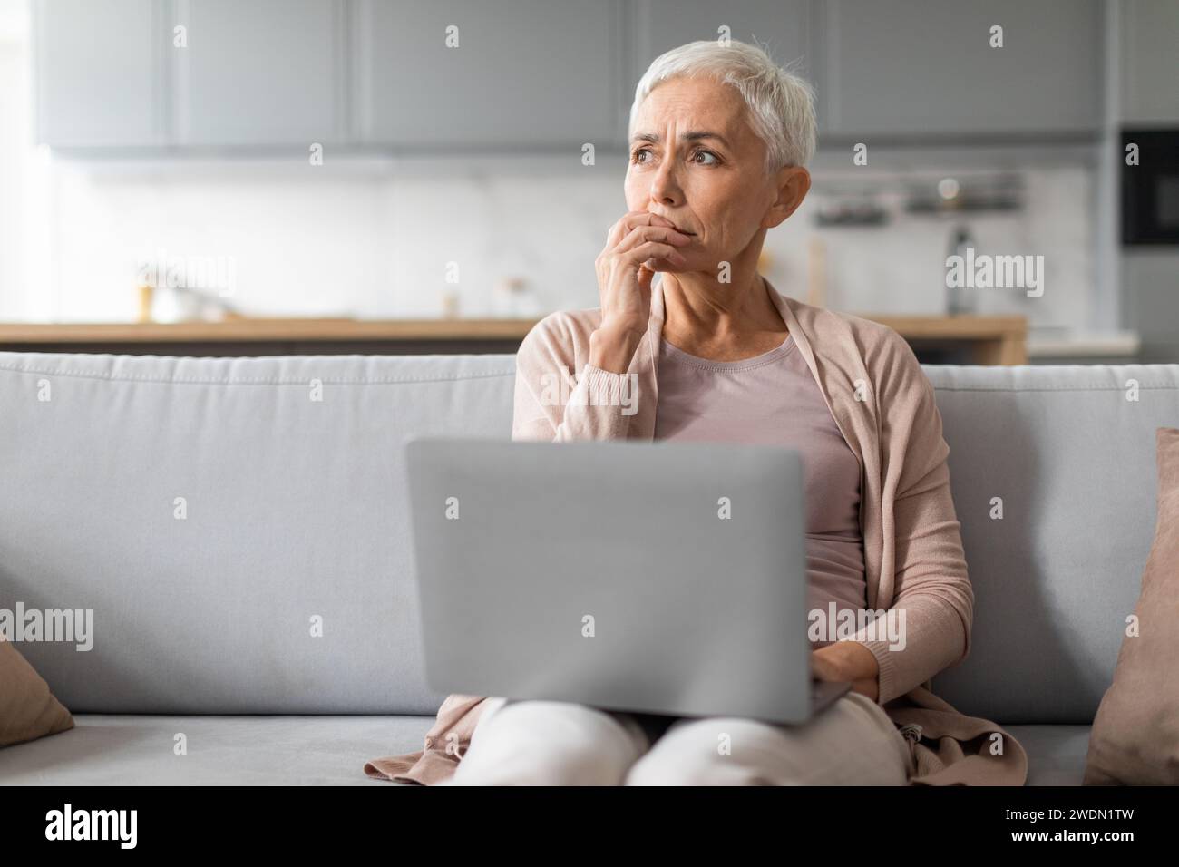 Concerned mature lady working on laptop thinking about issues indoor Stock Photo