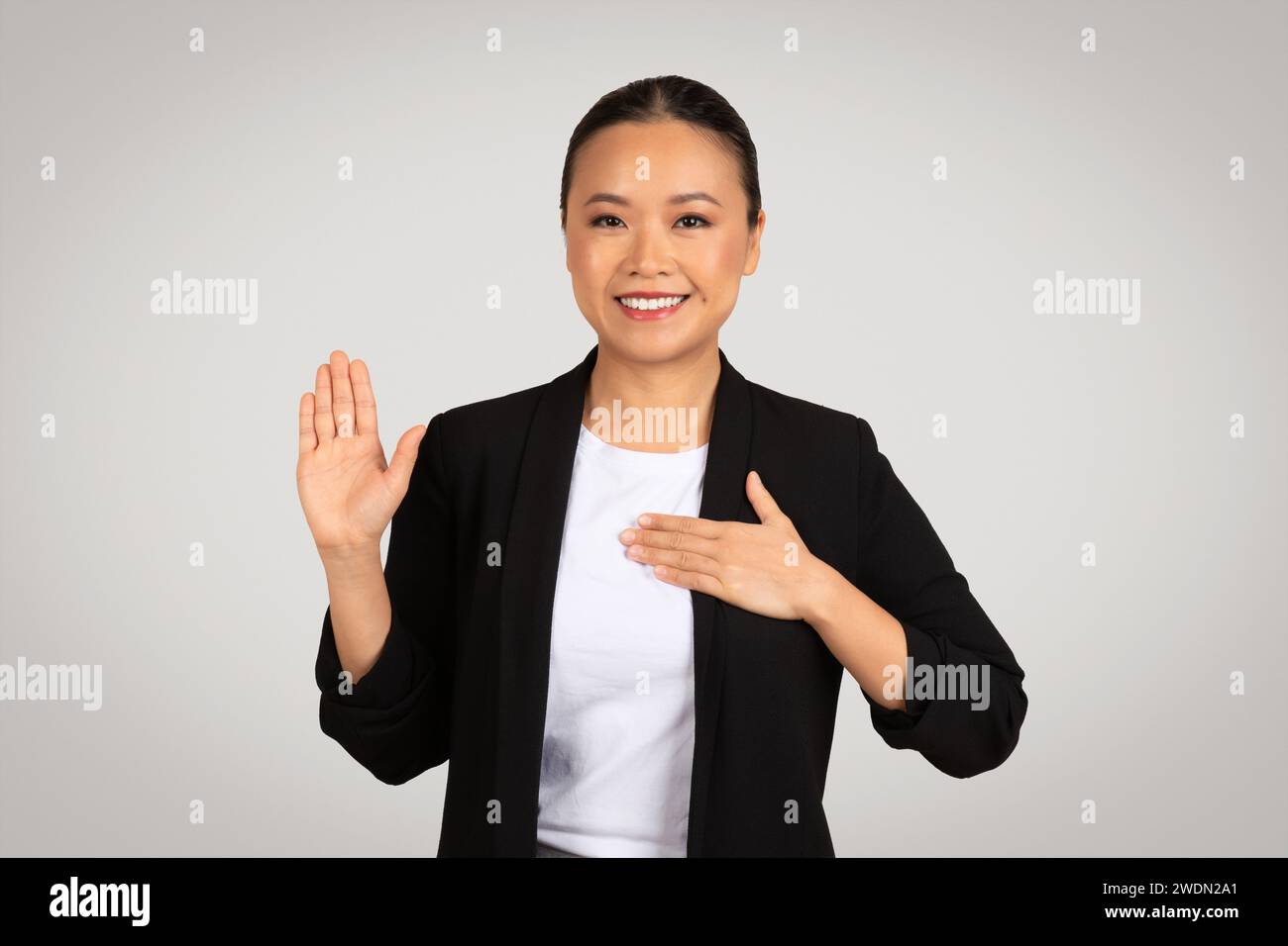 Professional Asian businesswoman making a pledge or oath gesture with a raised right hand Stock Photo