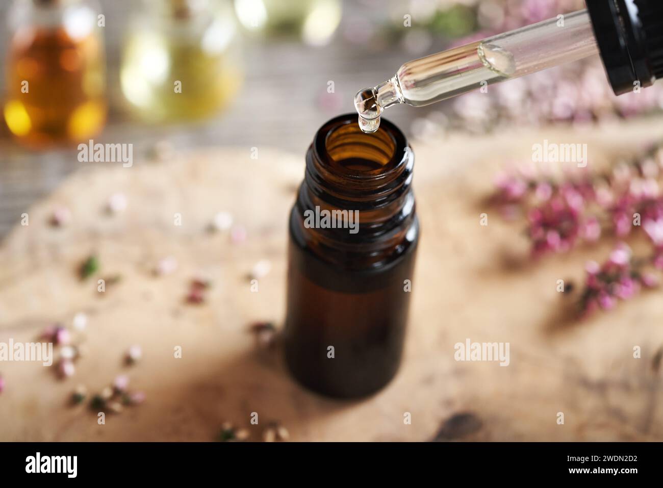 A drop of aromatherapy assential oil falling into a brown glass bottle on a table Stock Photo