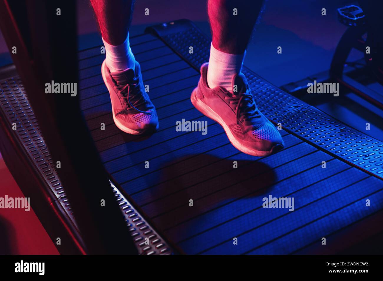 Close up on athletic footwear during a treadmill run, highlighted by dramatic blue and red gym lights amidst a misty ambiance Stock Photo