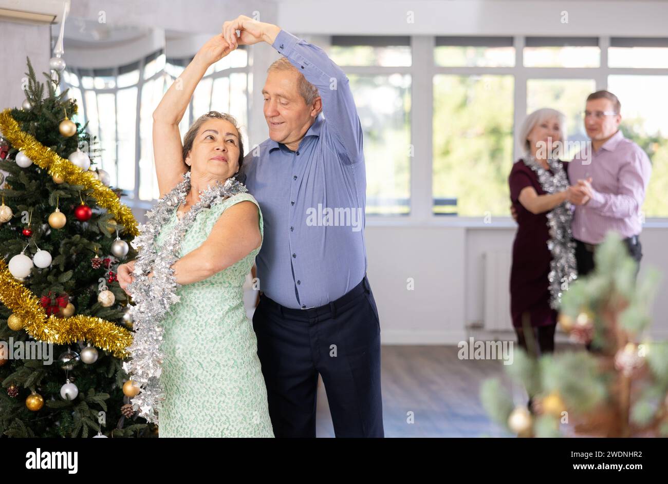 Smiling elderly woman and partner successfully perform mesmerizing movements of paso doble dance during celebration Christmas and New Year Stock Photo