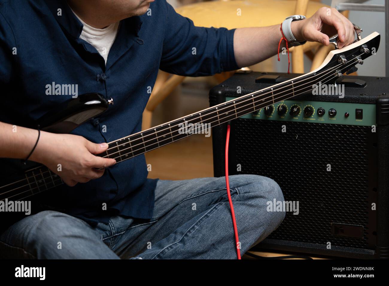 latin man tuning an electric bass next to an amplifier to start