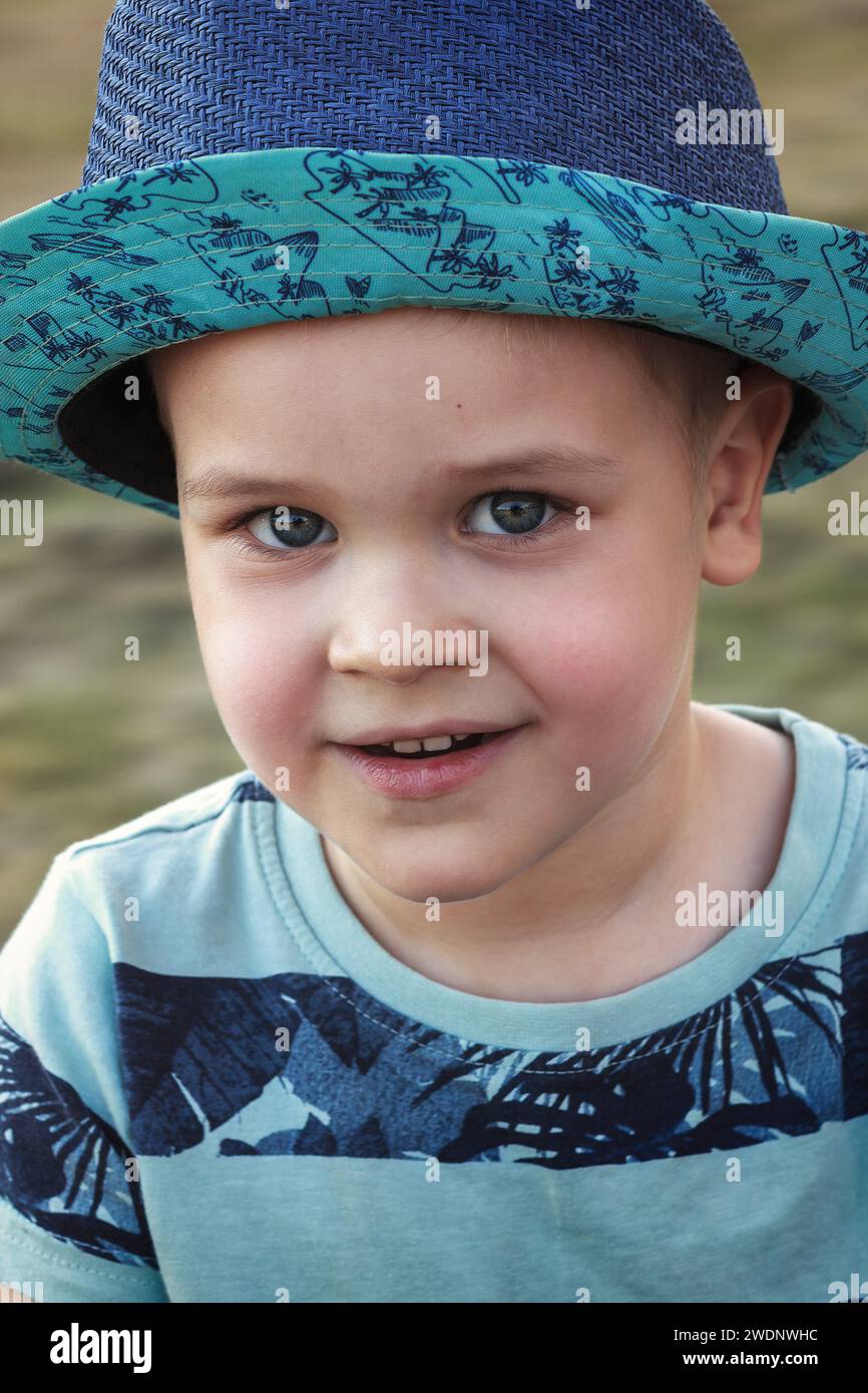 Close-up portrait of cute smiling boy in blue hat and blue clothes. Stock Photo