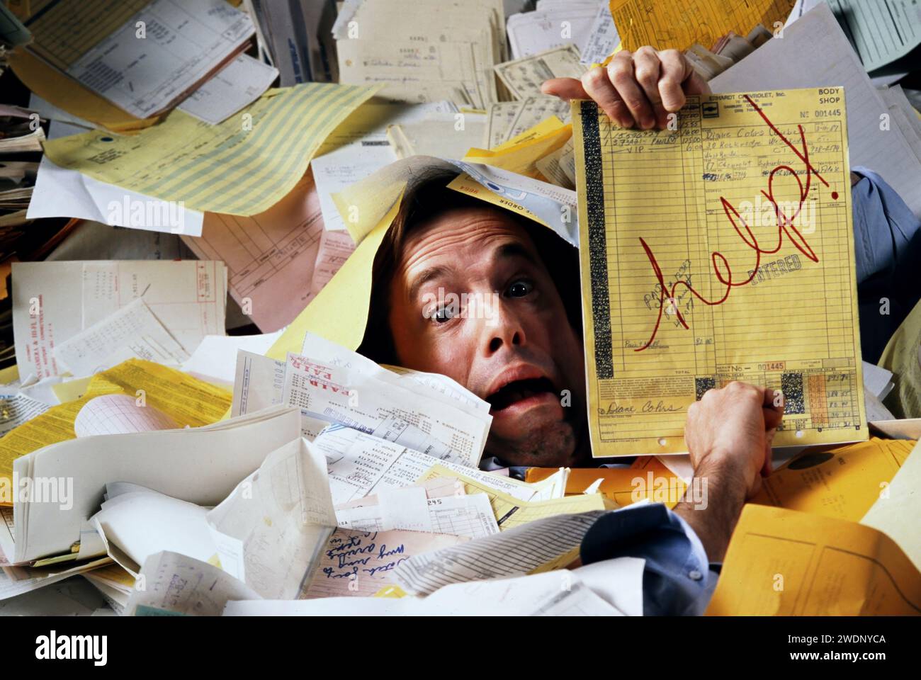 A businessman buried in a mountain of paperwork and asking for help Stock Photo