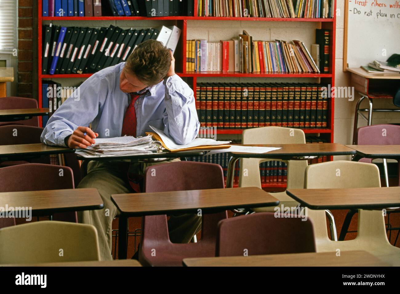 A teacher alone in his classroom grading papers while sitting at one of
