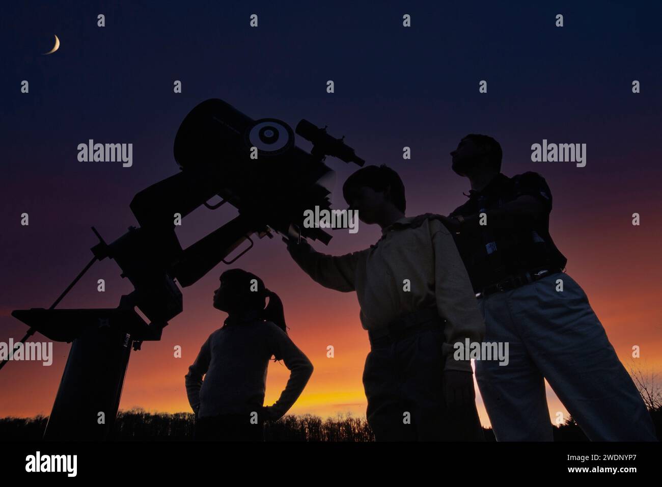 Oh father teaching his children about astronomy and the universe while looking at a crescent moon through a powerful telescope Stock Photo