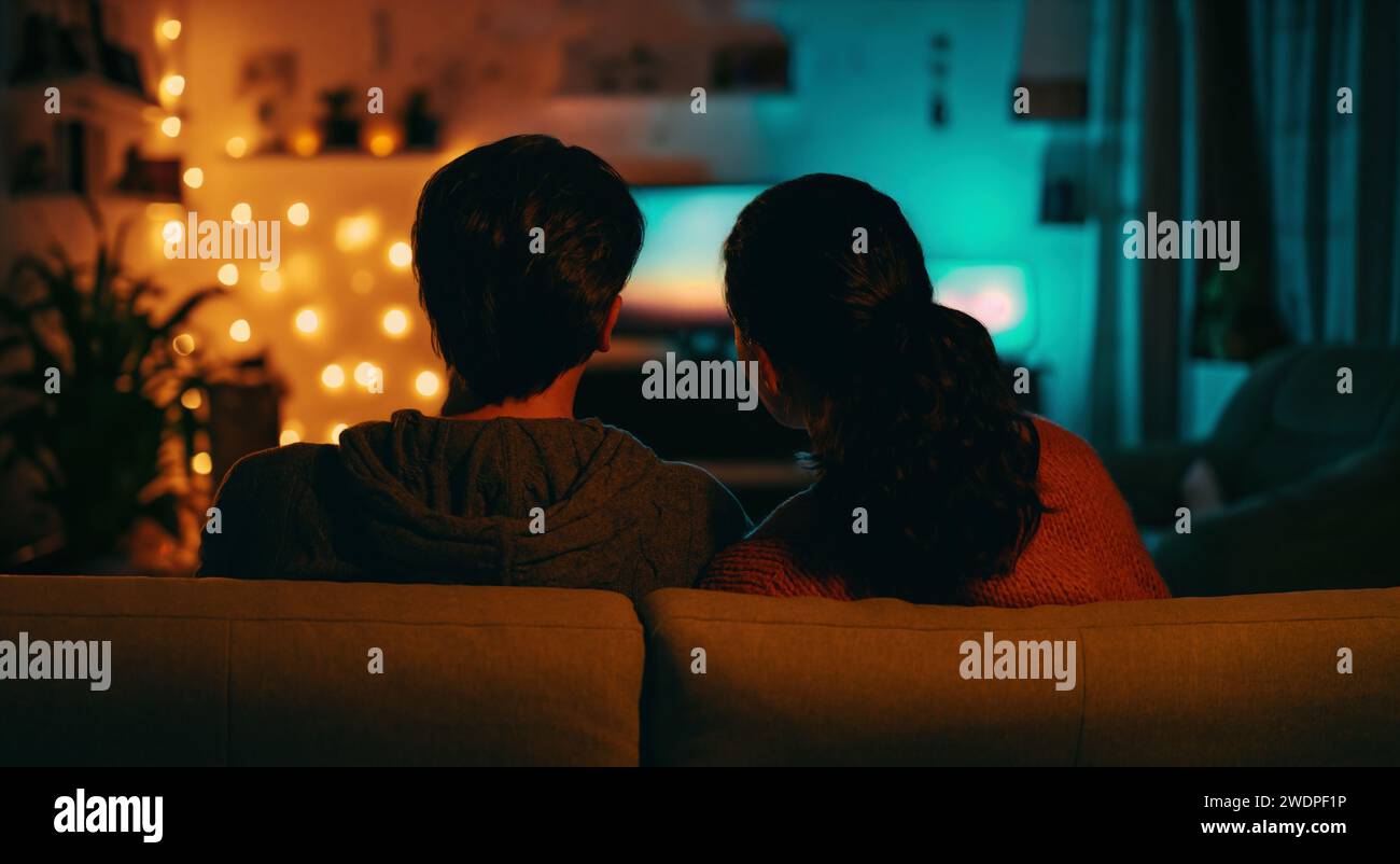 Happy family watching TV, movies in the evening at home. Couple spending time together. Stock Photo