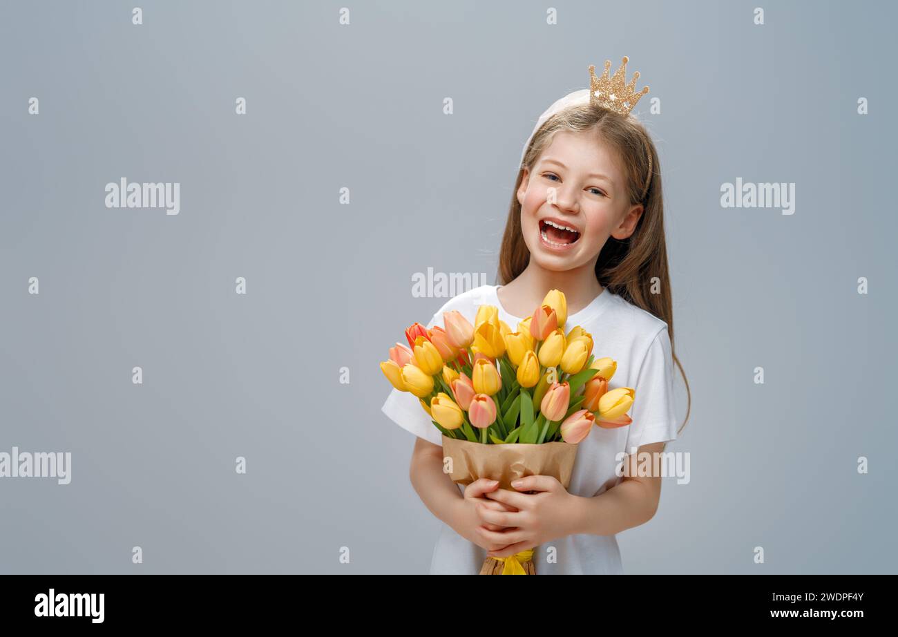 Beautiful girl with yellow flowers in hands on grey wall background. Stock Photo