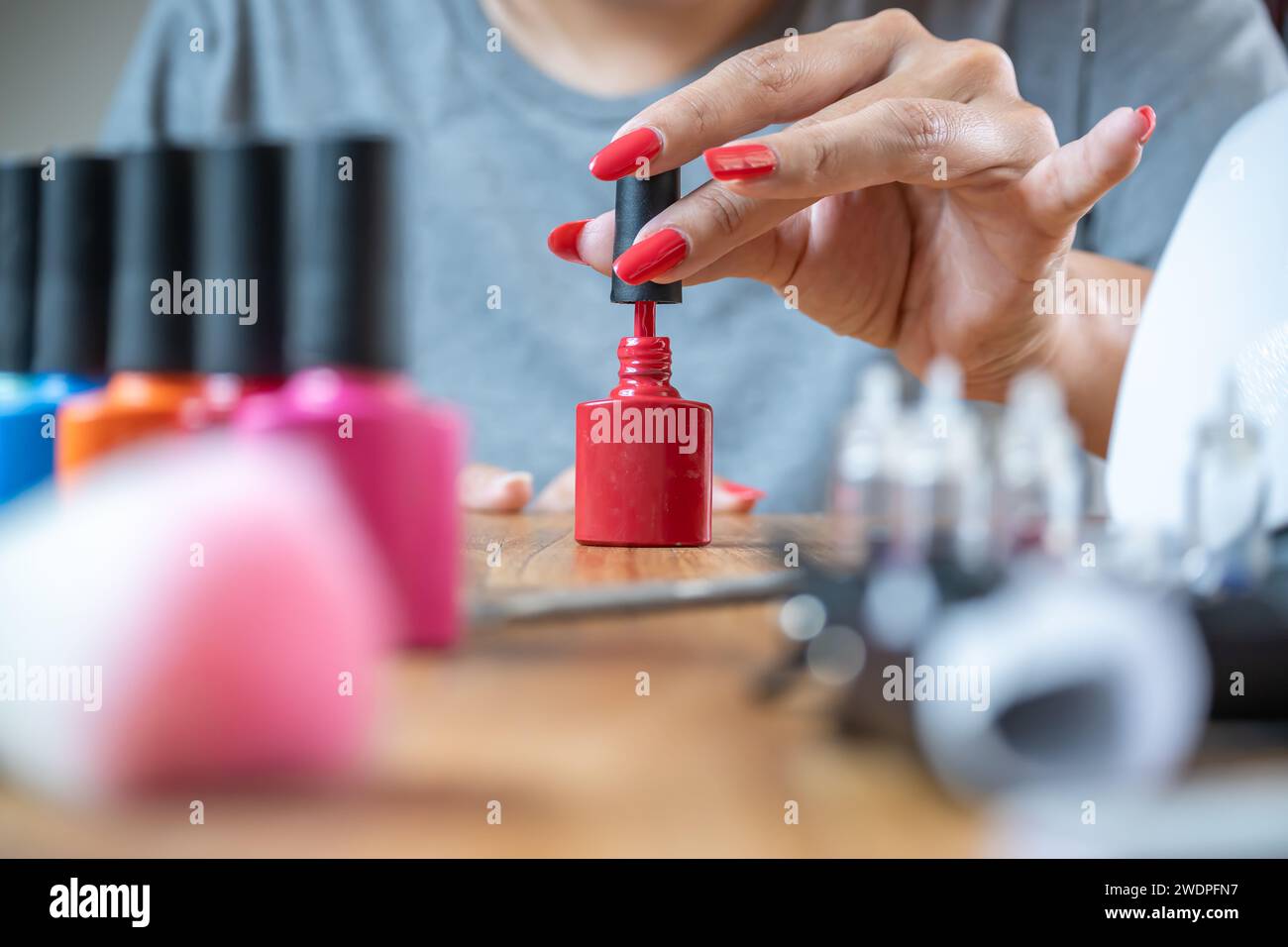 Young woman applies semi-permanent nail polish on a table full of nail art accessories. Stock Photo