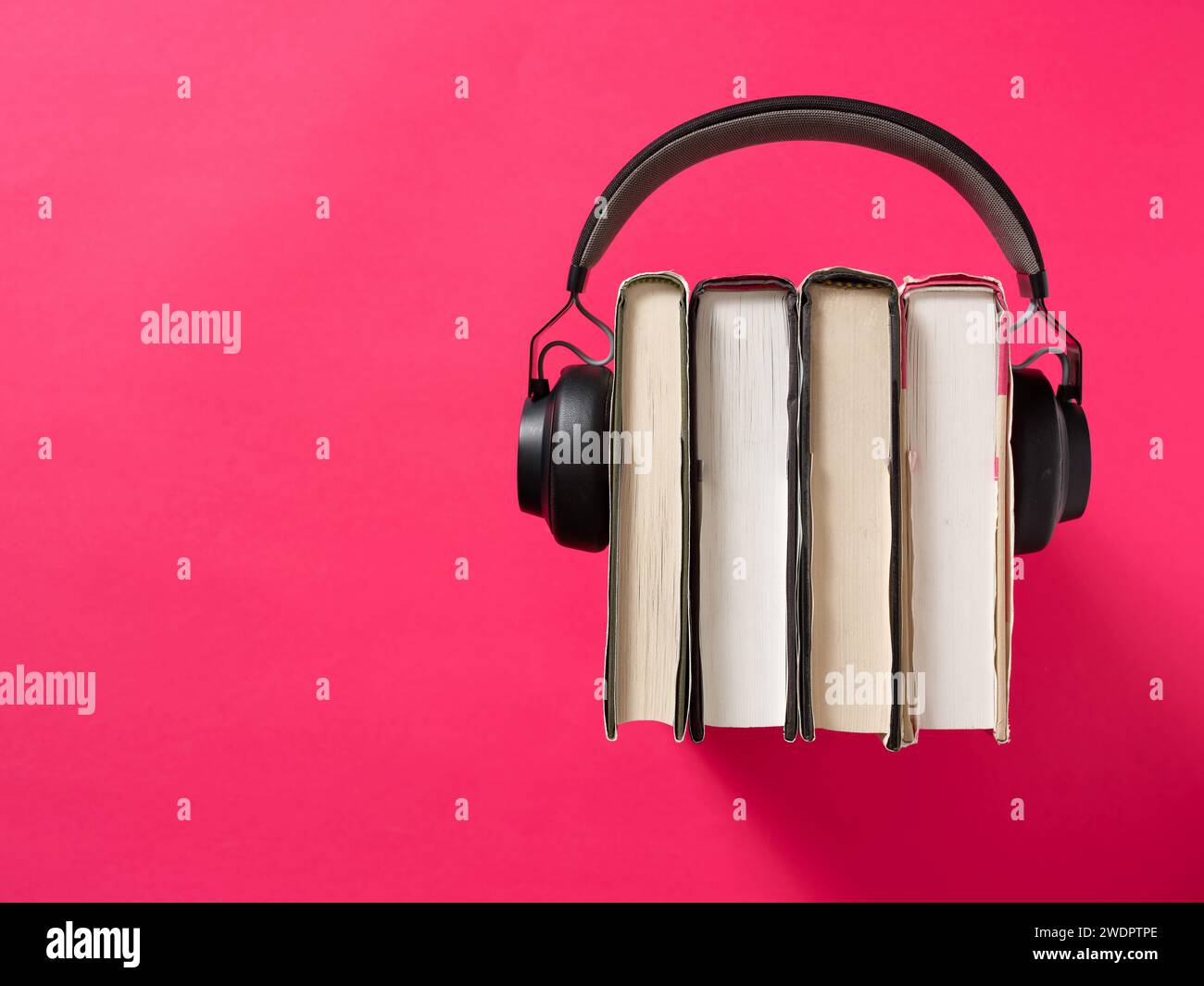 Audiobook concept. Online learning and education. Listen literature e-books in audio format. Headphone with stack of books on red background. Stock Photo