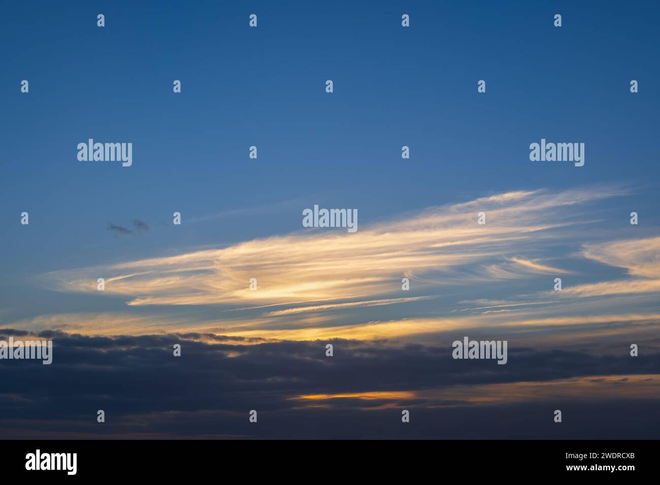 Sky at sunset background cloudscape with sunlit clouds and darker below. Stock Photo