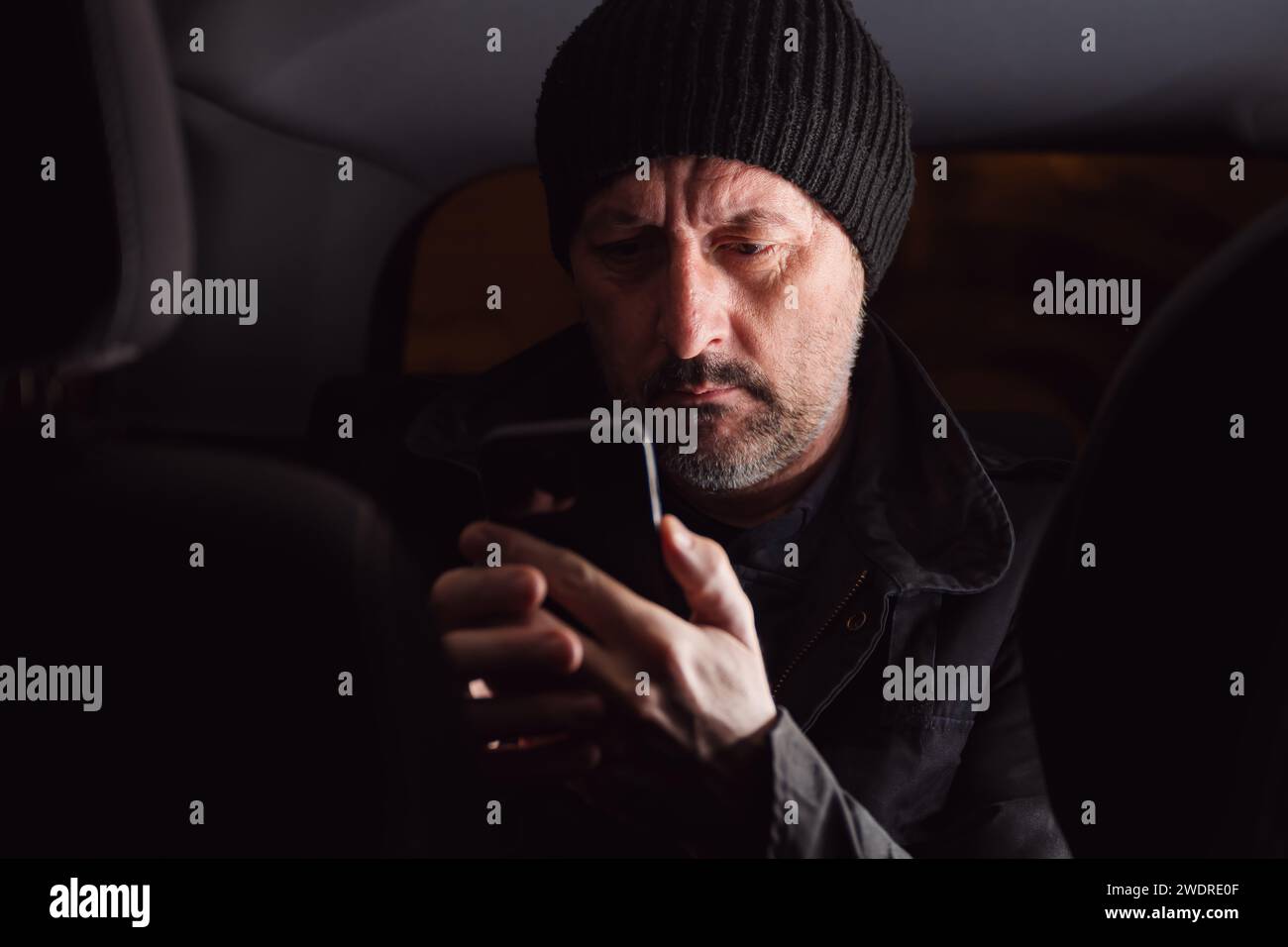Adult caucasian male reading text message on cellular phone while sitting at the back seat of the car at night, selective focus Stock Photo