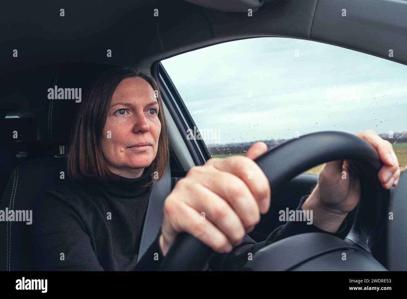 Caucasian female holding car steering wheel and driving through countryside landscape, selective focus Stock Photo