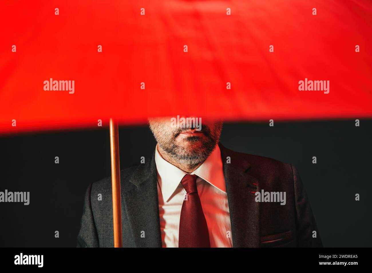 Businessman under red umbrella, low key with selective focus Stock Photo