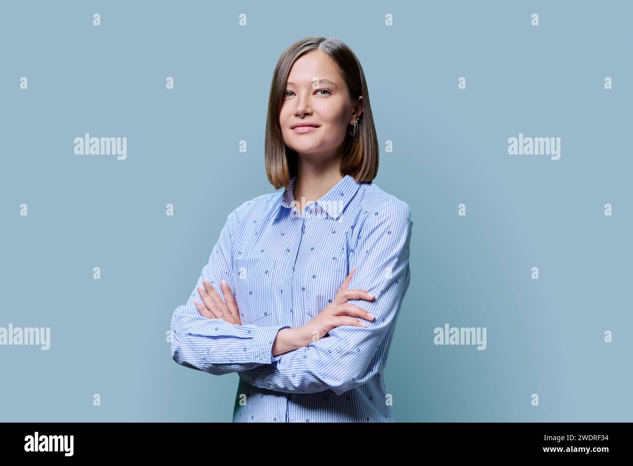 Portrait of confident young woman with crossed arms on blue background ...