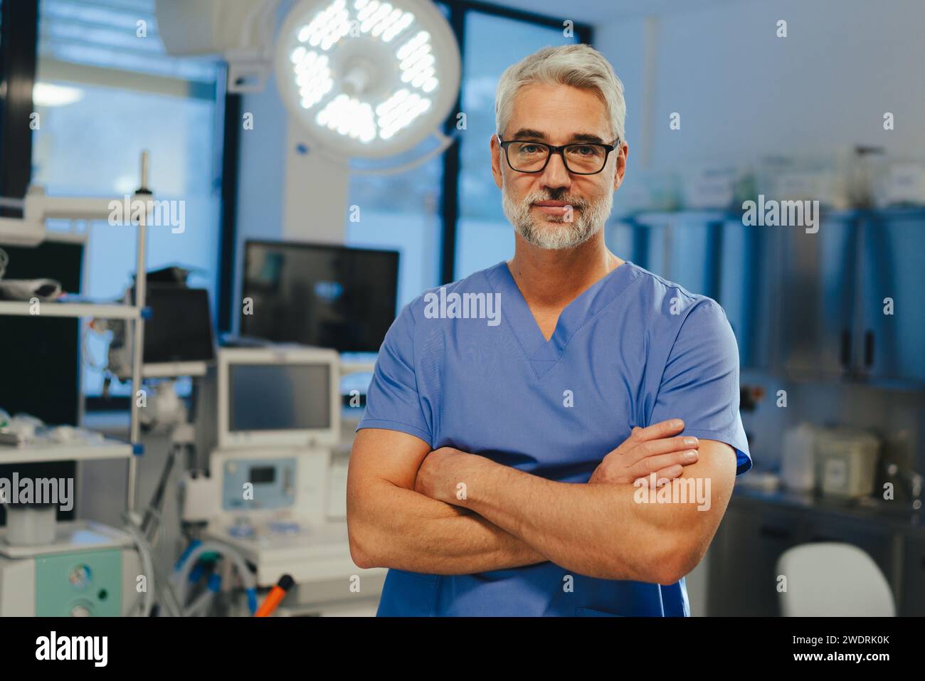 Portrait of confident ER doctor standing in hospital emergency room. Handsome doctor in scrubs holding clipboard, standing in modern private clinic. Stock Photo