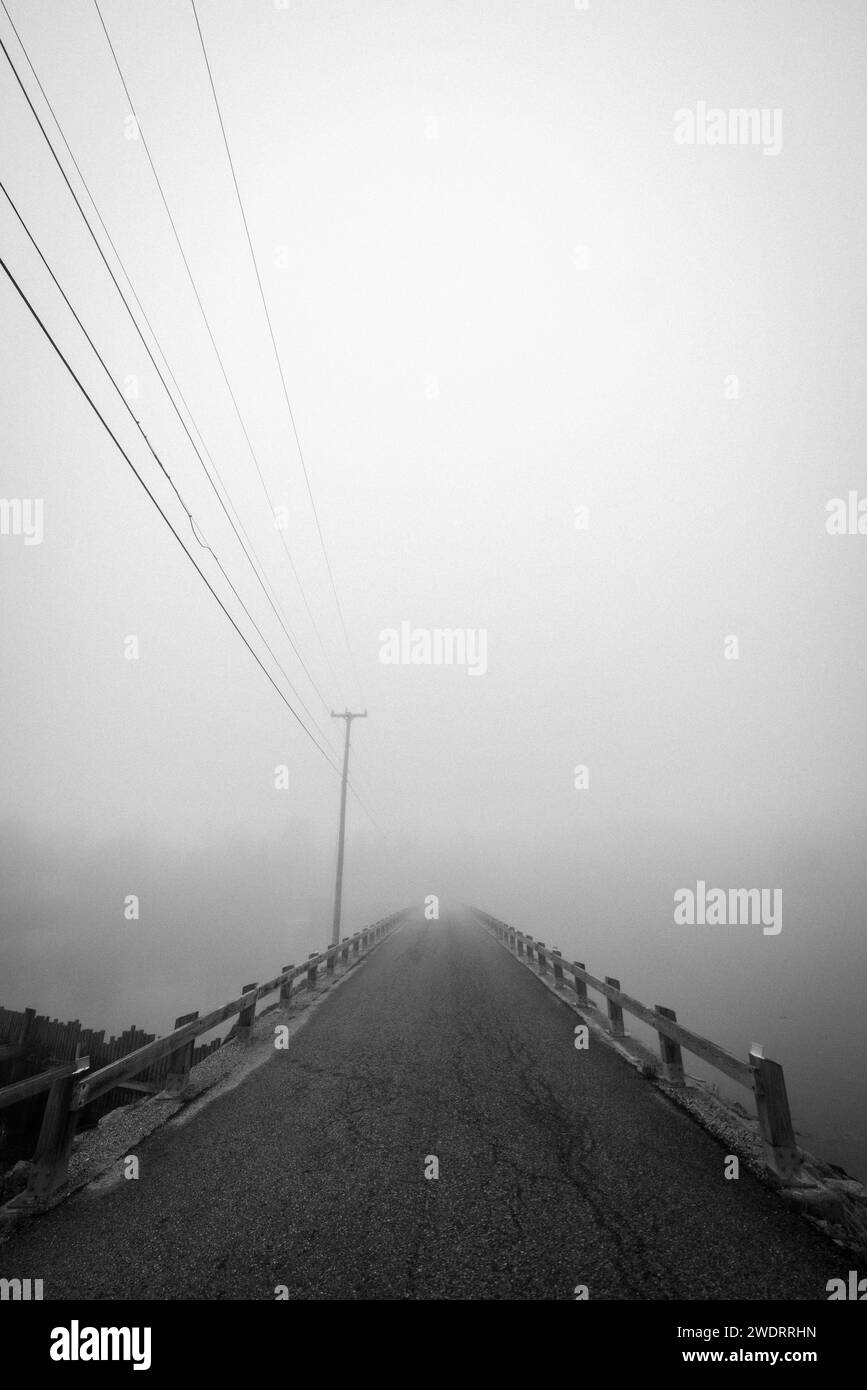 causeway with powerlines recedes into heavy fog, Maine Stock Photo