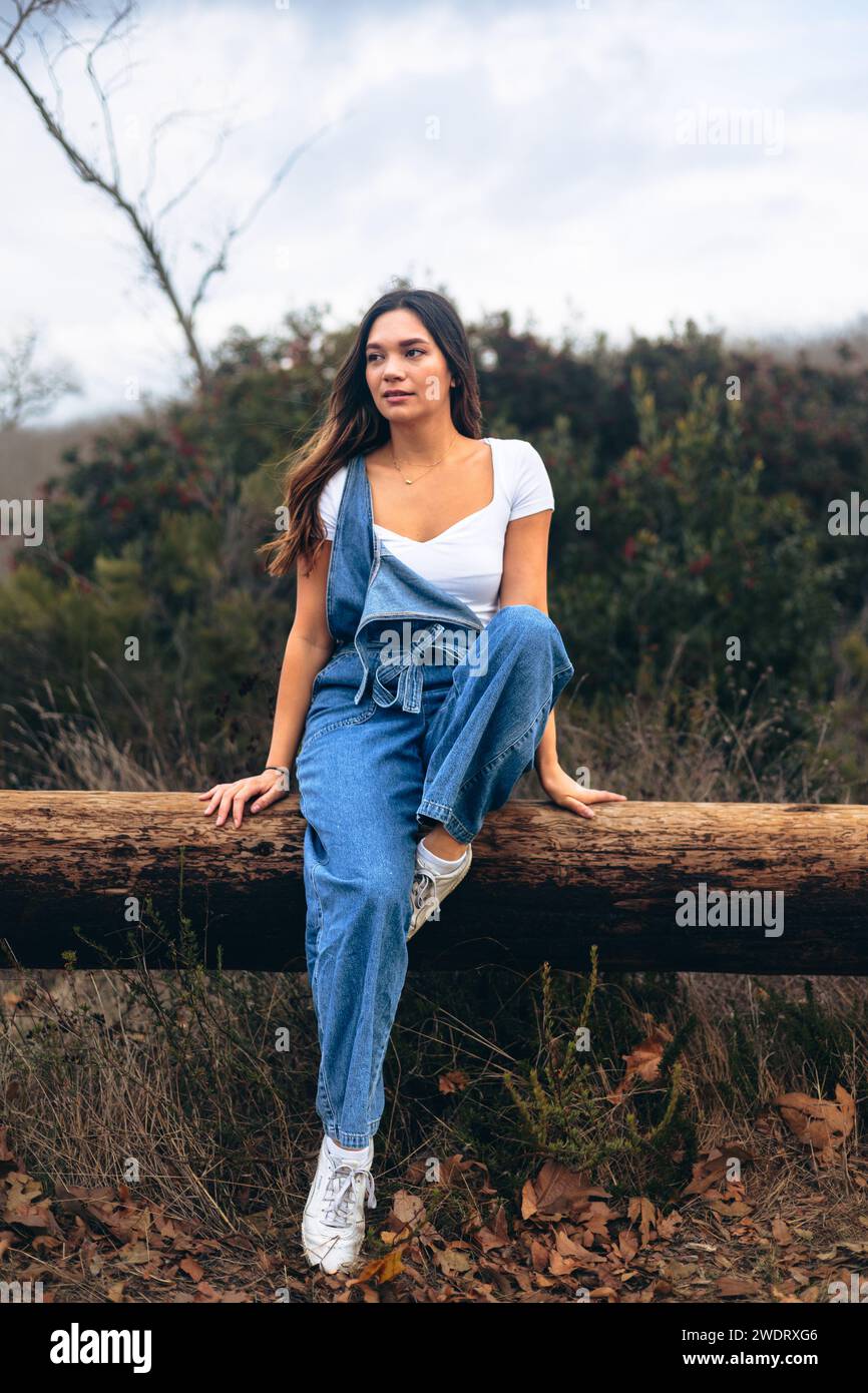 Young woman sitting on log on hiking trail looking to background Stock Photo