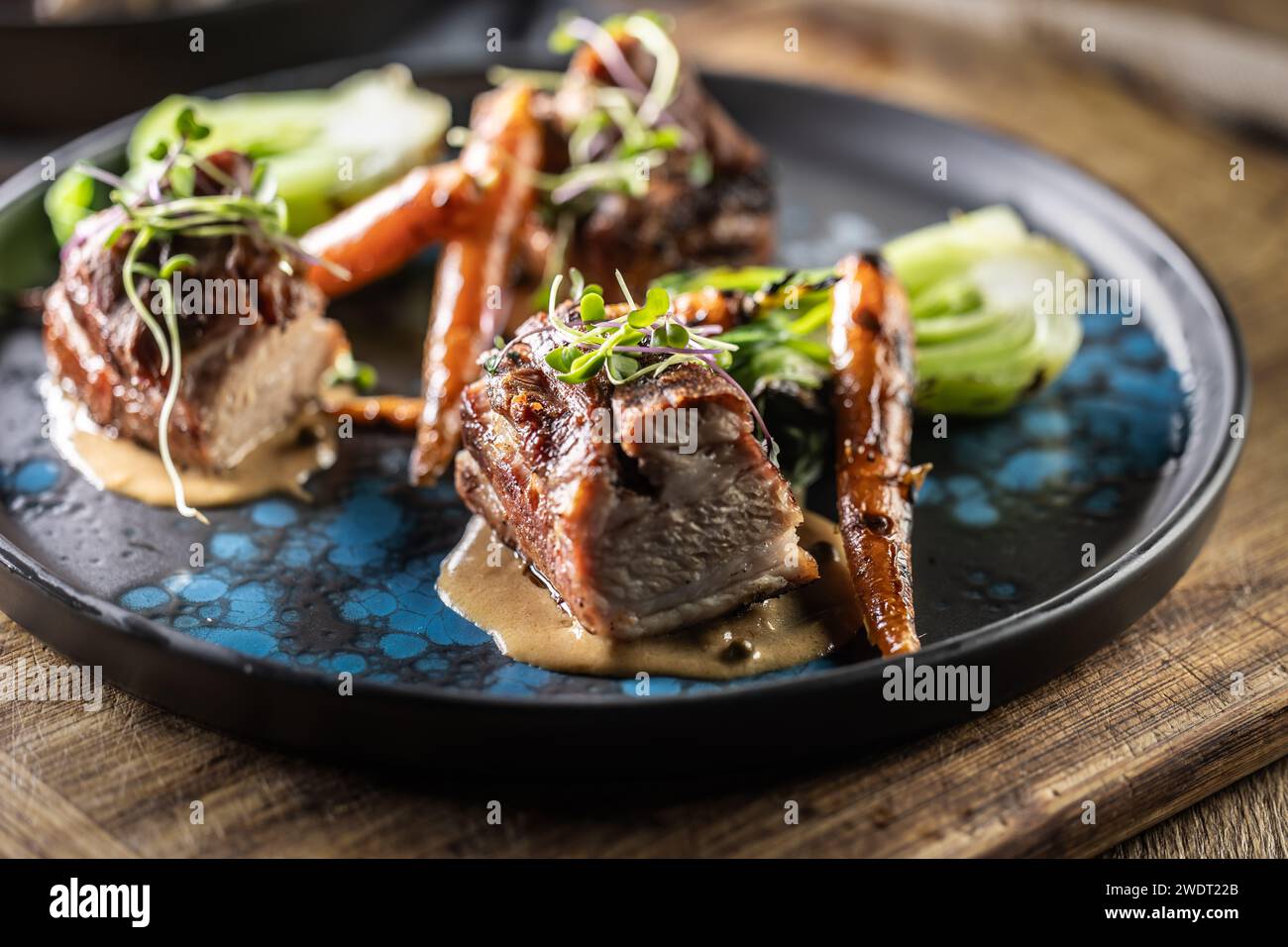 Three pieces of baked belly with grilled vegetables on a plate in a pub or restaurant. Stock Photo