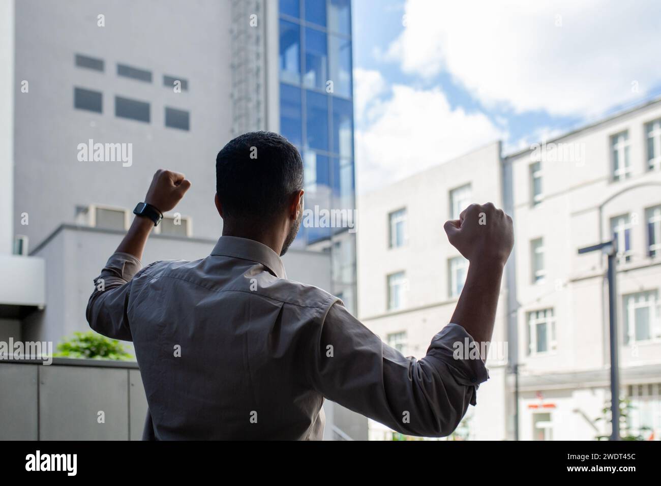 Energized African American young man in shirt showing victory gesture, feeling triumphant near office. Stock Photo