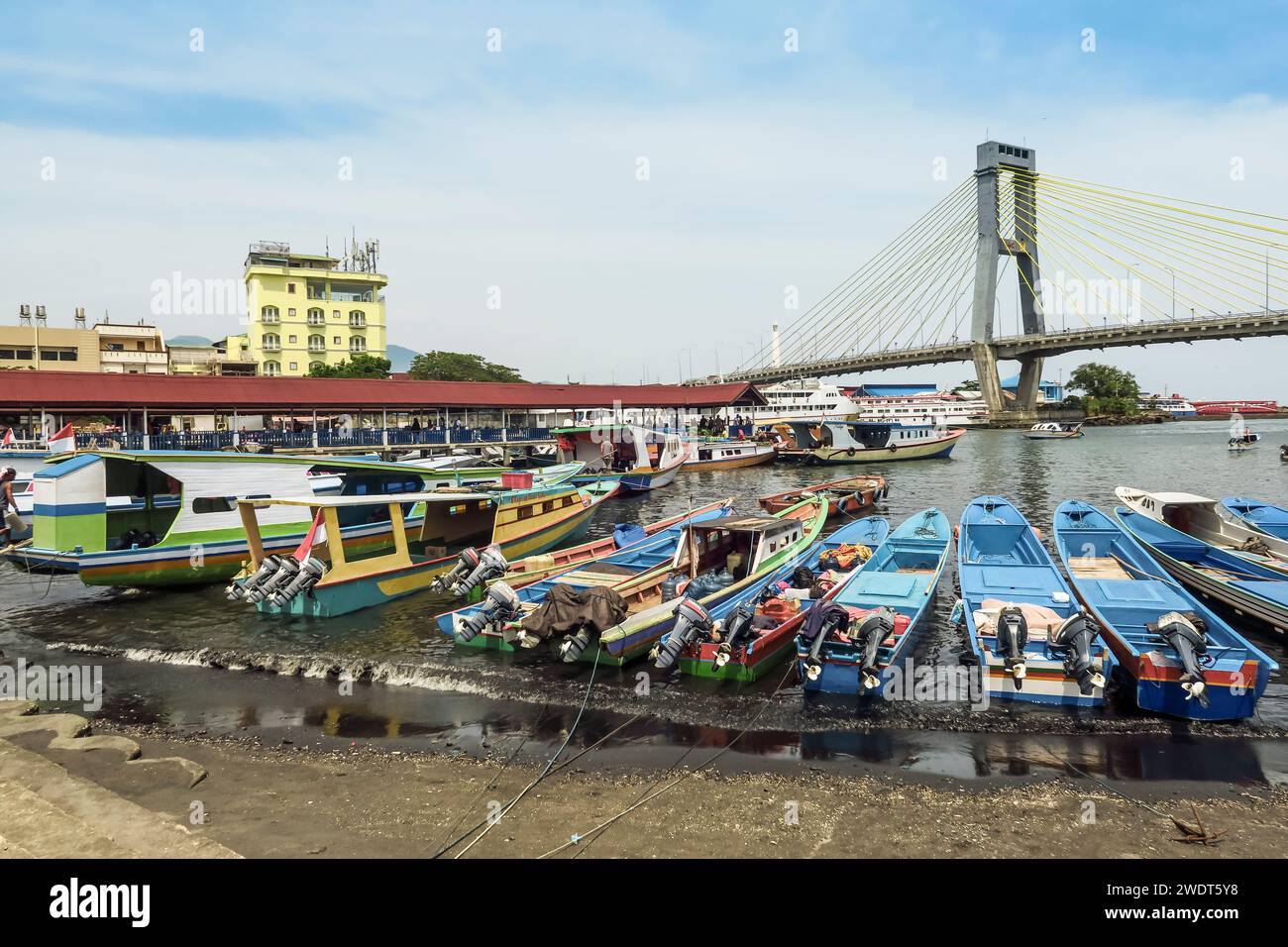 Typical ferry boats in Manado port with the Soekarno Bridge beyond in provincial capital of Sulawesi's far north, Manado, North Sulawesi, Indonesia Stock Photo