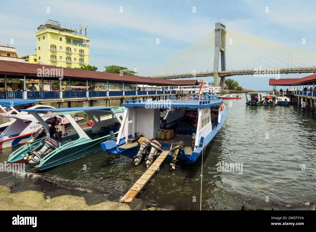 Covered ferry boats in Manado port with Soekarno Bridge beyond in provincial capital of Sulawesi's far north, Manado, North Sulawesi, Indonesia Stock Photo