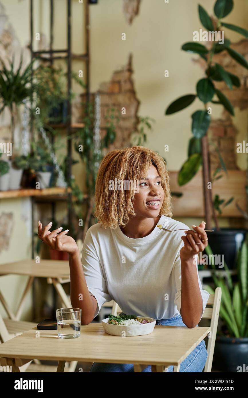 jolly african american girl in braces eating fresh salad in bowl inside