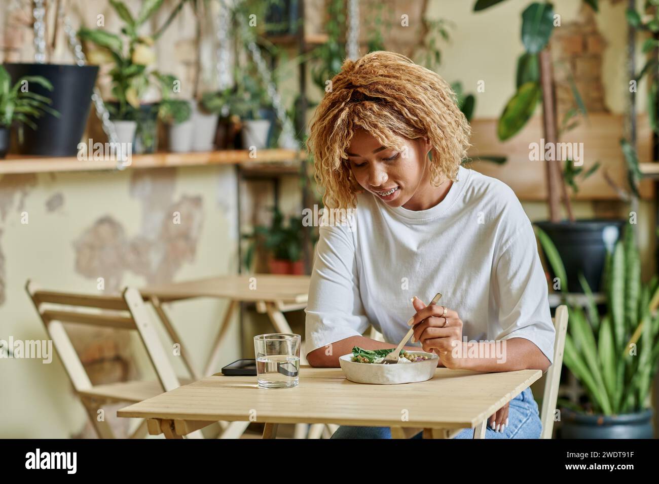 young african american woman in braces eating fresh salad in bowl