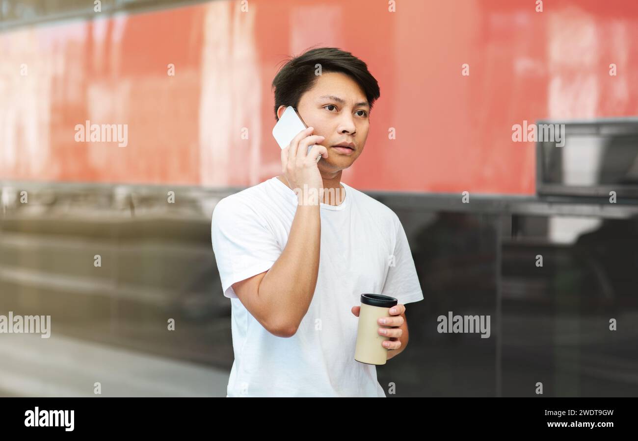 Concentrated asian guy talking on phone, drinking coffee Stock Photo