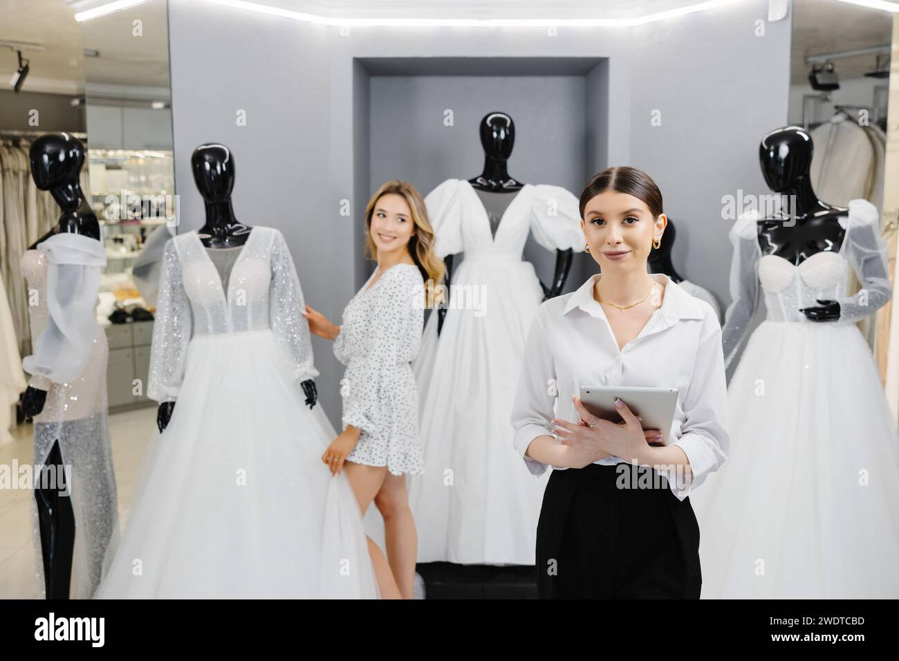 Attractive bridal shop owner women use digital tablet help customer choosing wedding gown at the store. Stock Photo