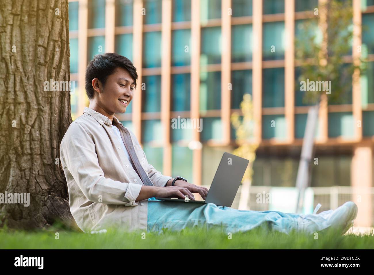Relaxed young asian guy freelancer working at park Stock Photo