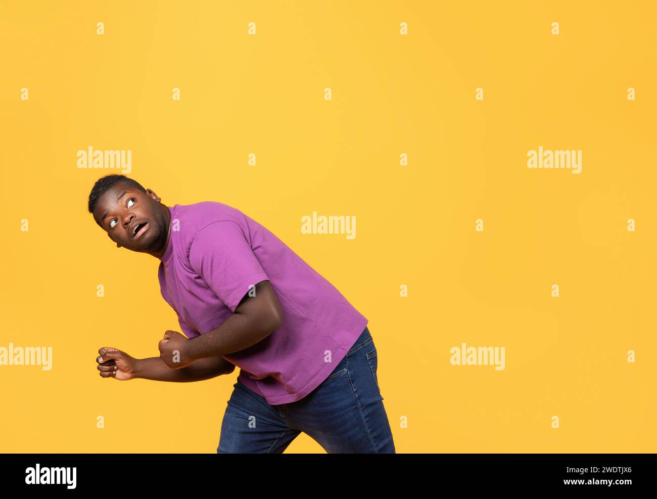 Scared black man bending down in defensive pose, yellow backdrop Stock ...