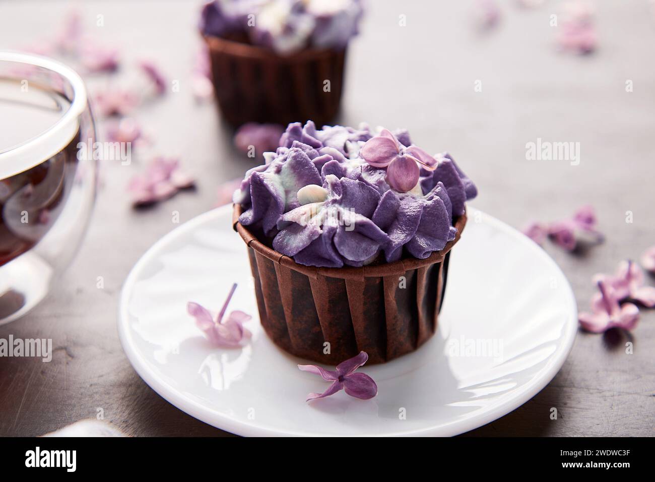 Floral purple cupcake close up using trend Dreamy Escapism. Desserts, coffee and lilac flowers background. Aesthetics food. Stock Photo