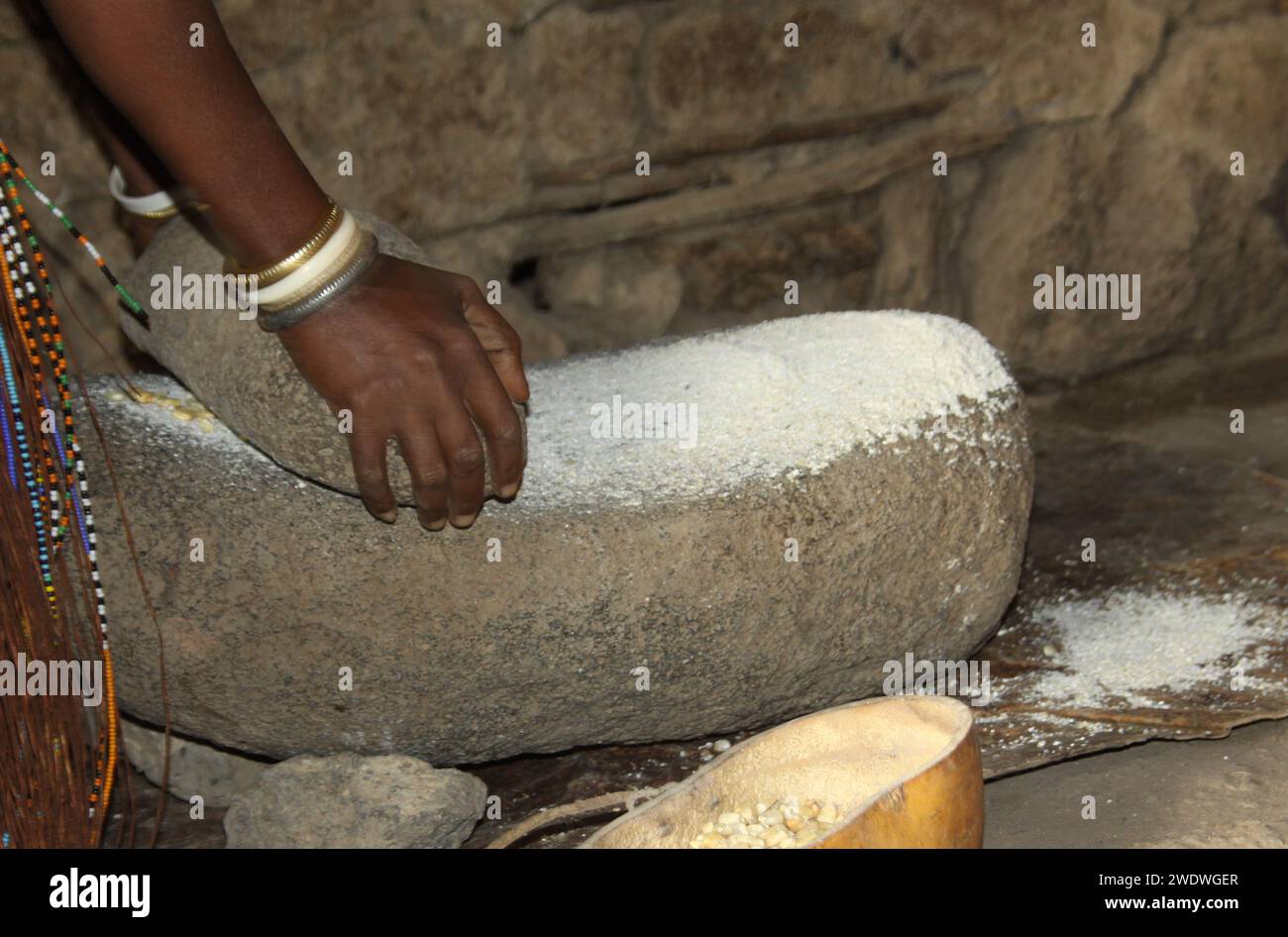 Datoga woman in traditional leather dress adorned with beads and brass bracelets milling grain to flour. Stock Photo
