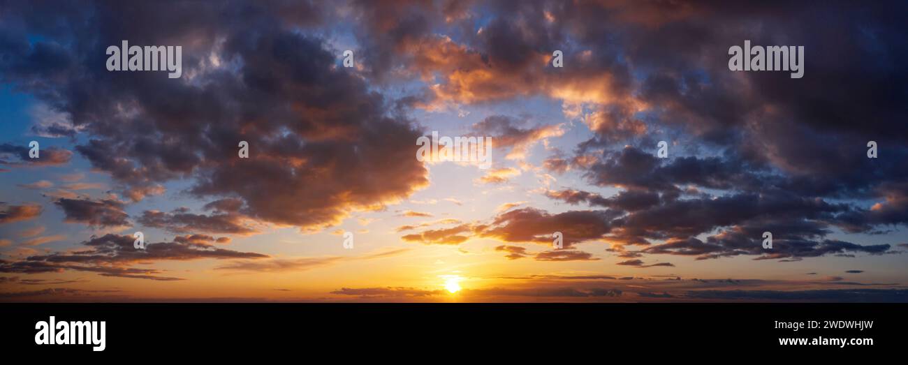 Dramatic sunset sky with clouds. Beautiful natural panorama of cloudy sky with setting sun. Stock Photo