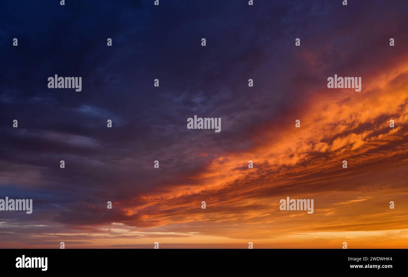Vibrant sunset sky background with dark clouds illuminated by orange sunlight. Stock Photo