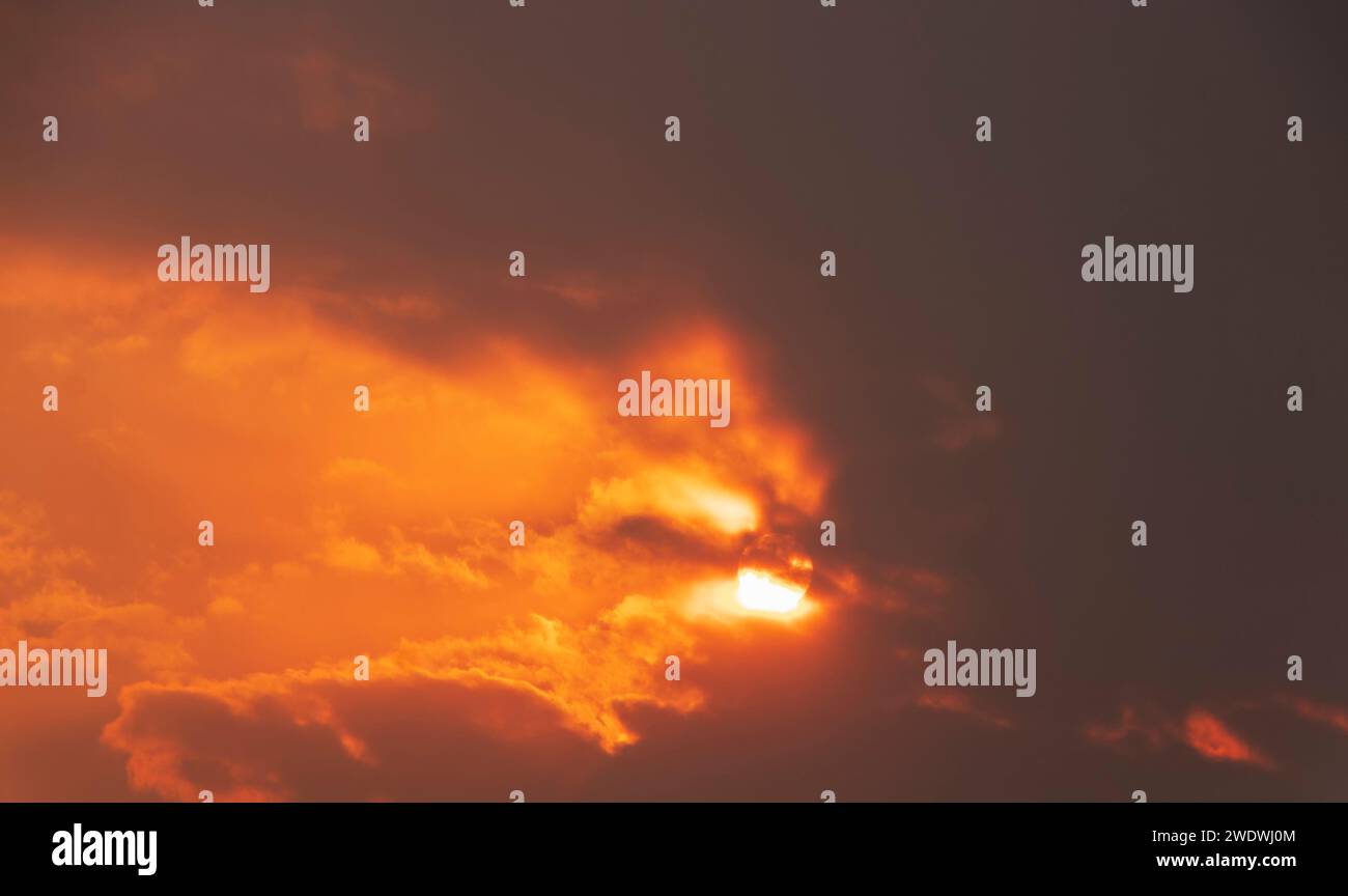 Dramatic sunset sky with bright sun shining through the dark clouds. Stock Photo