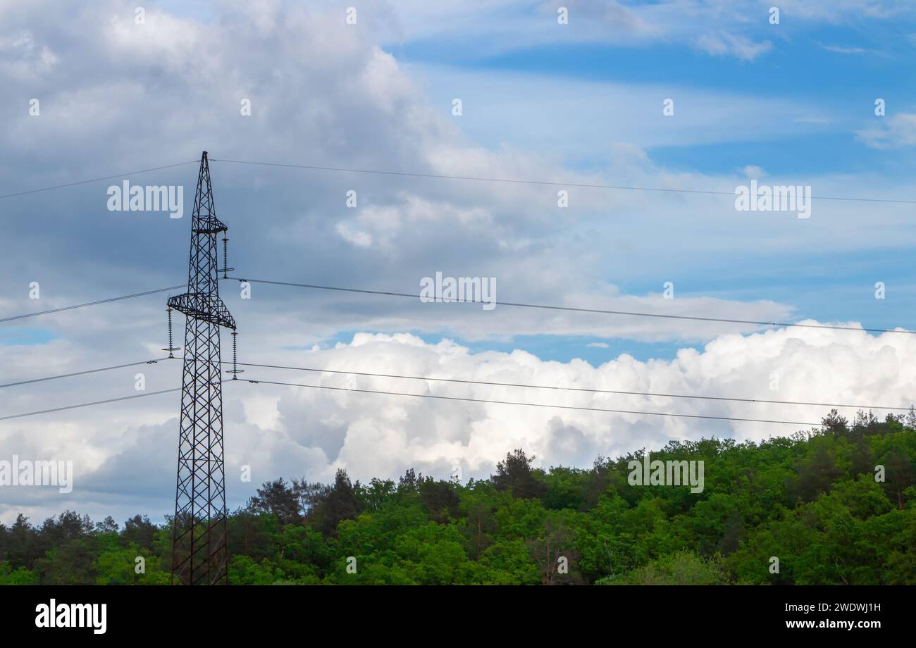 High voltage pole with wires against a cloudy sky and forest Stock Photo