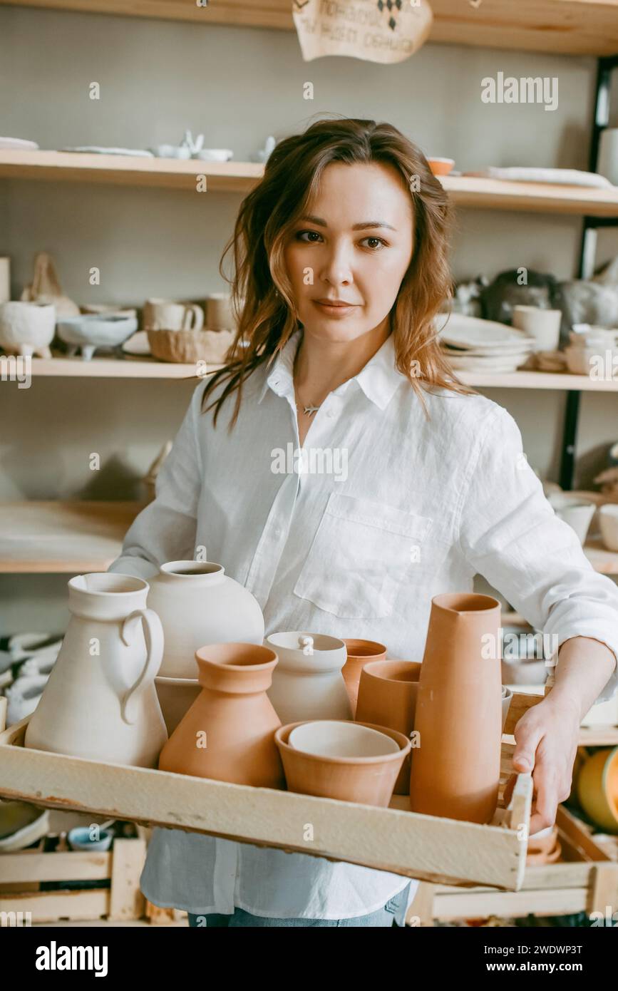 Woman master of pottery workshop carries clay products for firing Stock Photo