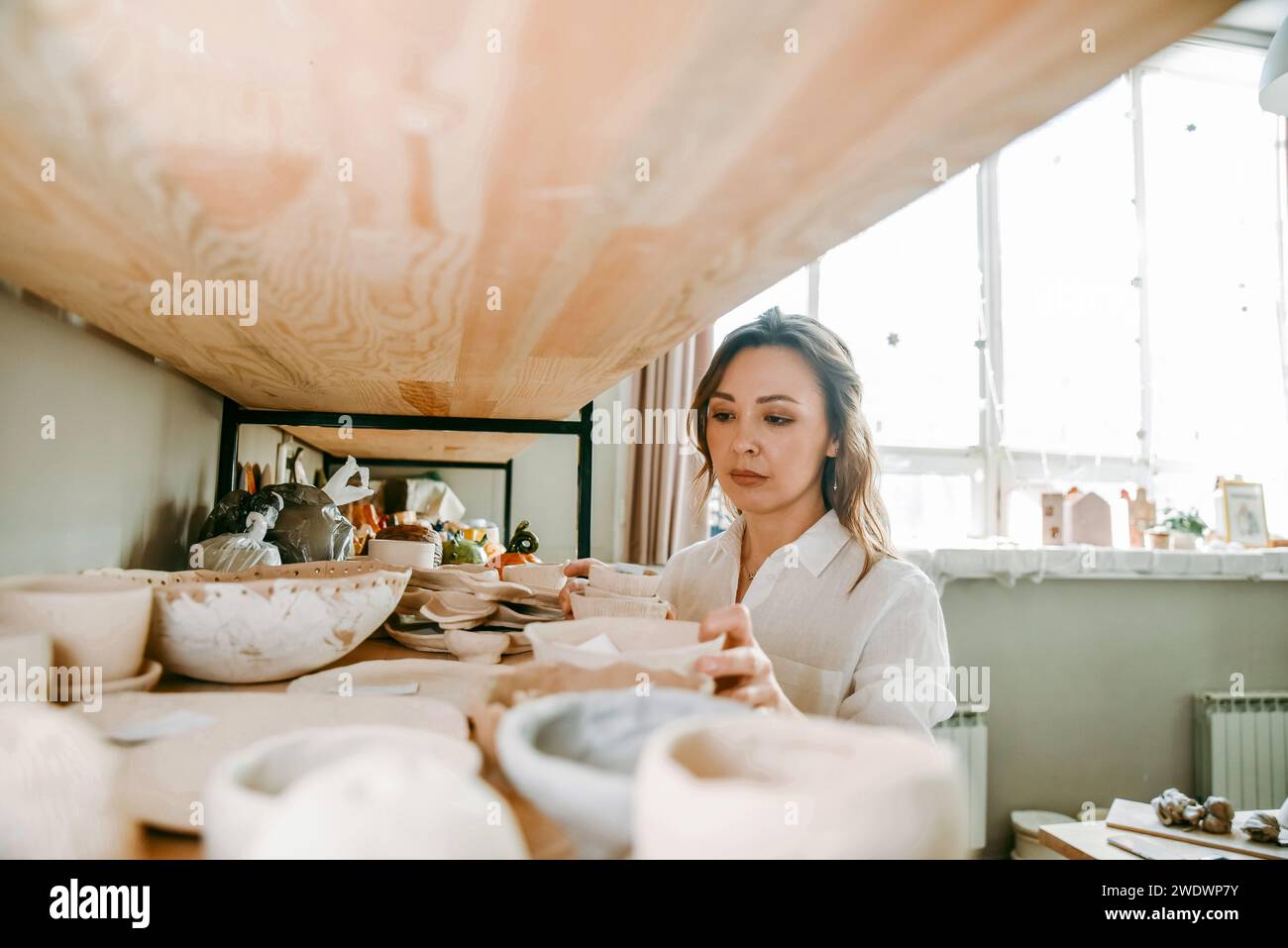 Young woman manager of pottery workshop arranges products on shelf Stock Photo