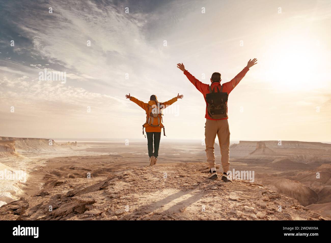 Two young hikers with backpacks are standing with open arms against valley and enjoys sunset Stock Photo