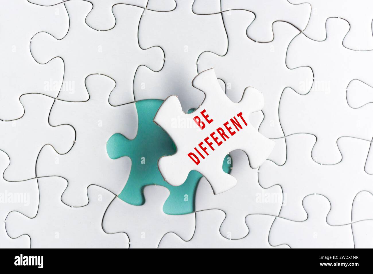 Be different text on white Jigsaw Puzzle over green background. Stock Photo