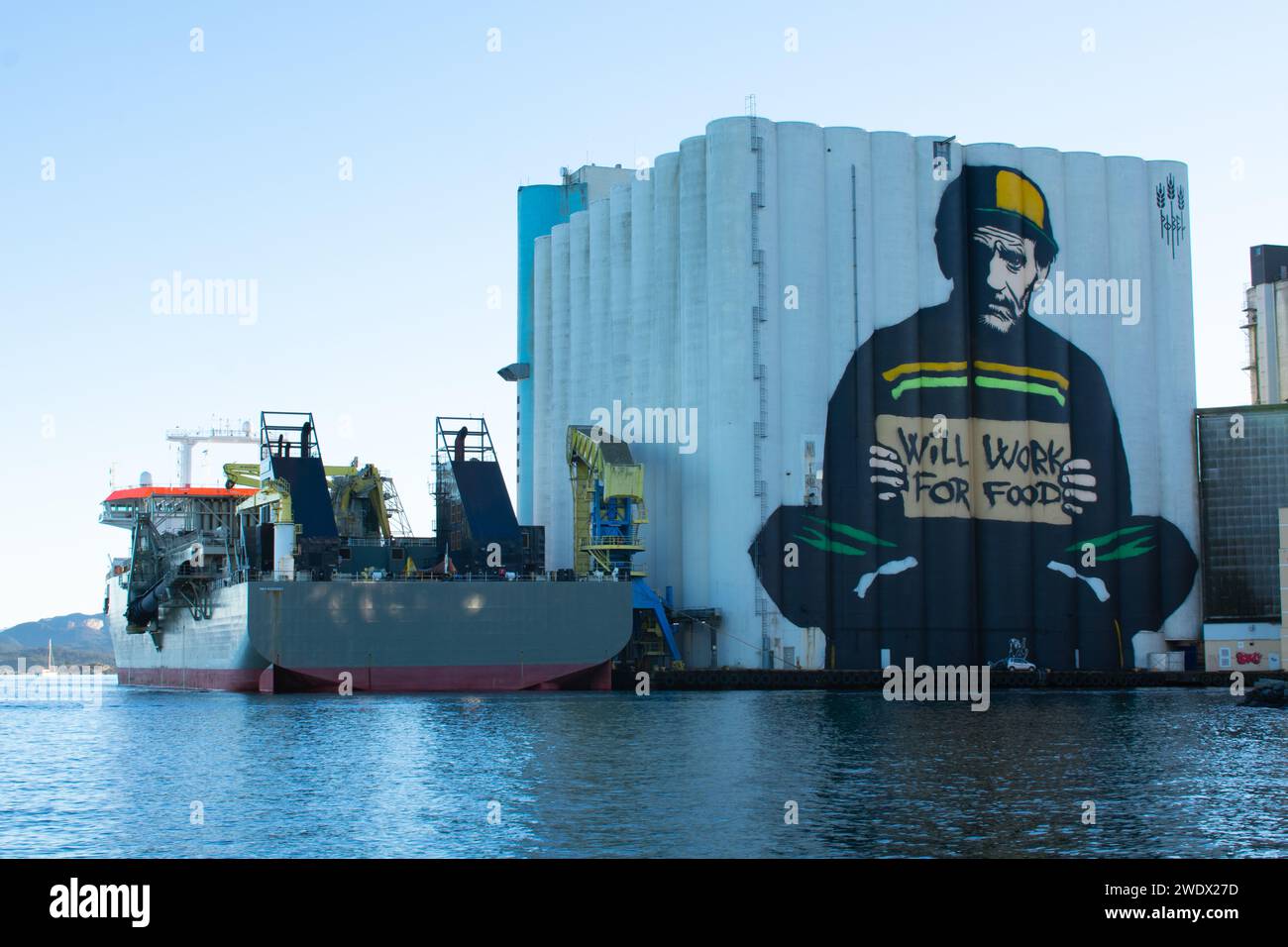 Will Work For Food graffiti. Large graffiti painted onto working silos next to ocean. Rogaland Norway Stock Photo