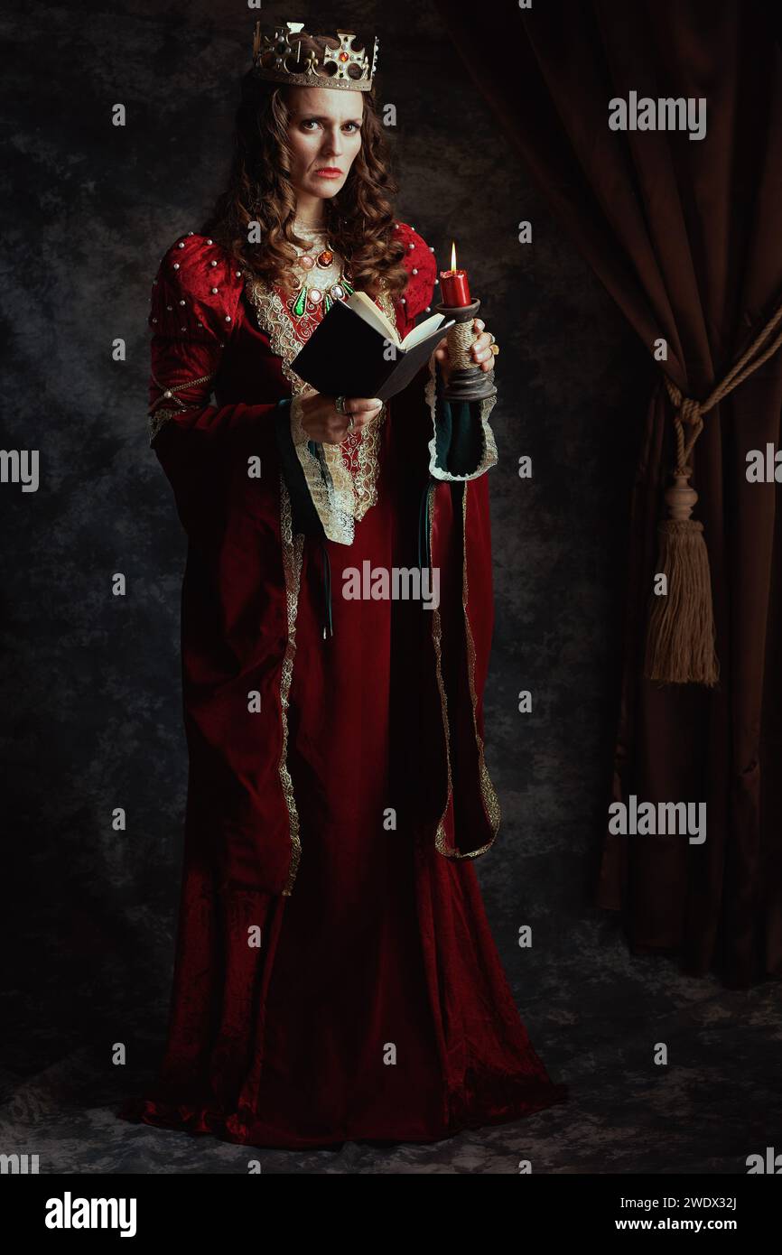Full length portrait of medieval queen in red dress with book, candle ...
