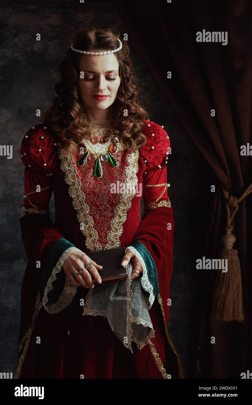 medieval queen in red dress with book and handkerchief on dark gray ...