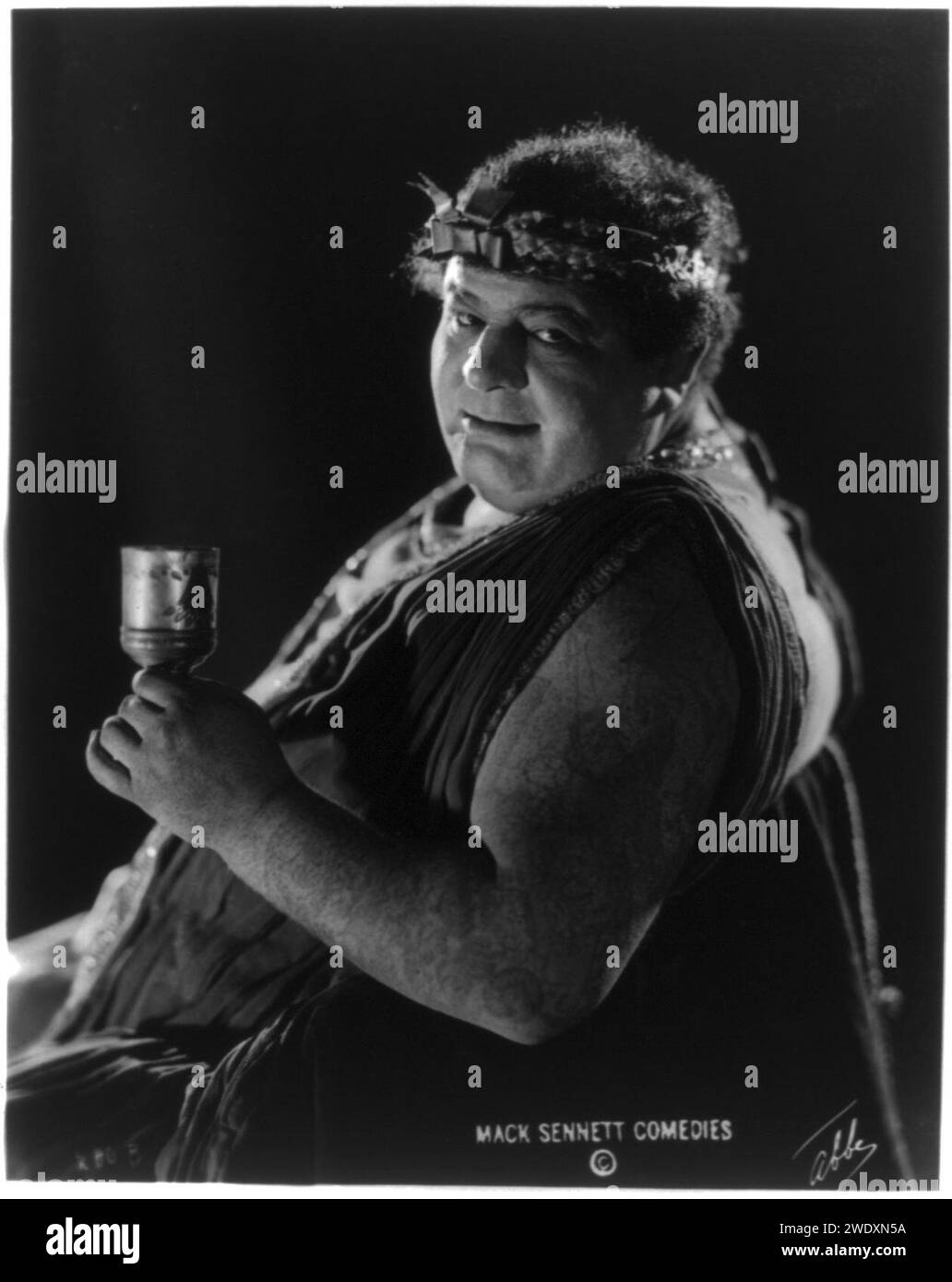 Actor from Mack Sennett comedy film in Roman toga seated holding wine glass) - Abbe Stock Photo