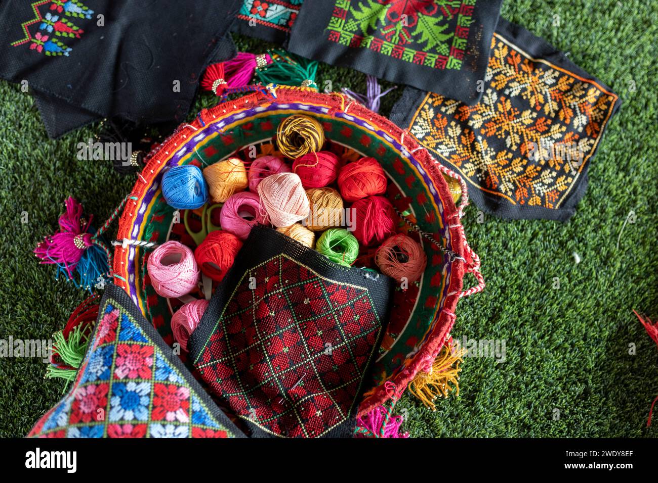Embroidery and multi-colored balls of thread in a wicker basket on the table. Stock Photo