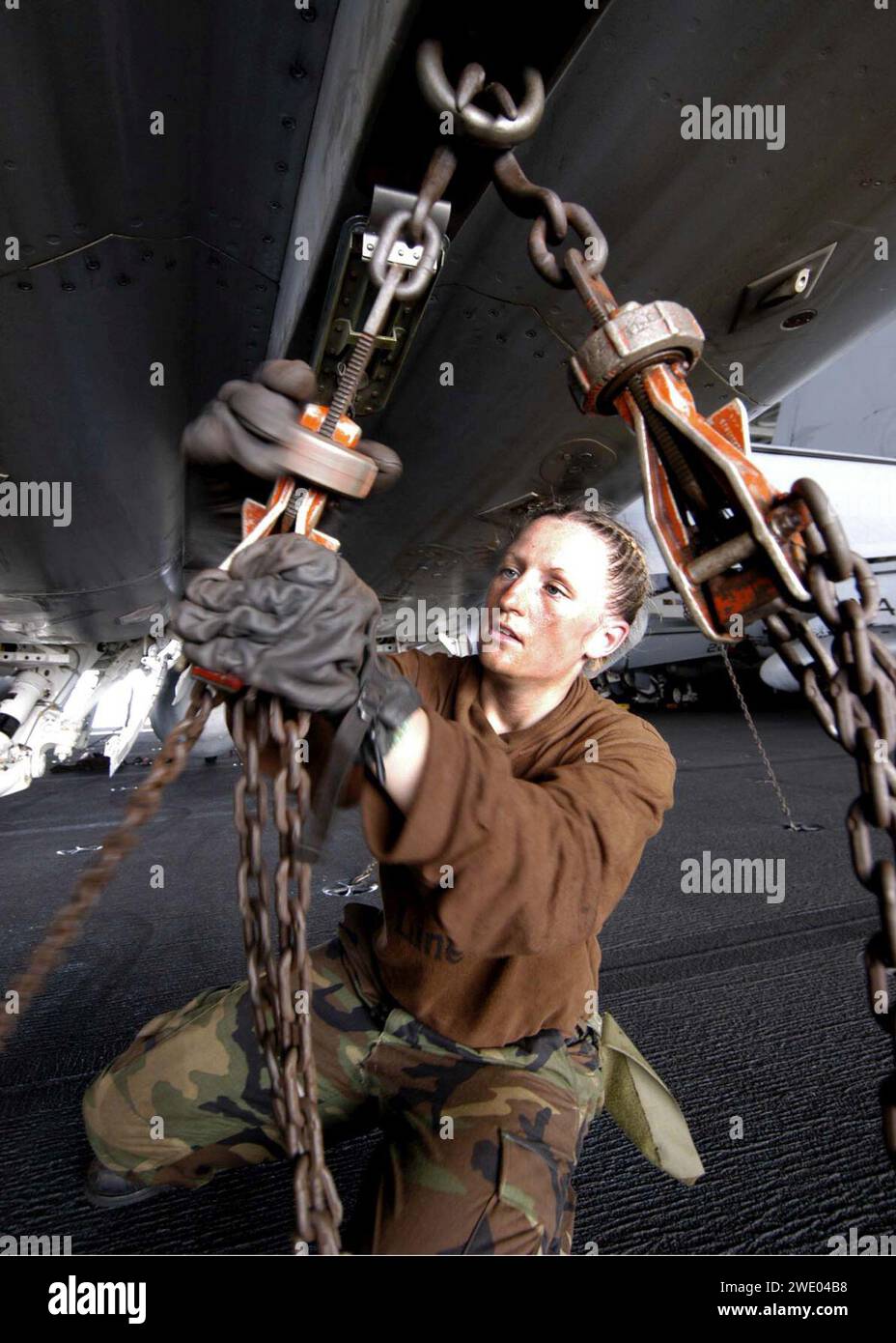 Airman Jolenea Pederson tightens a tiedown chain on an FA18E